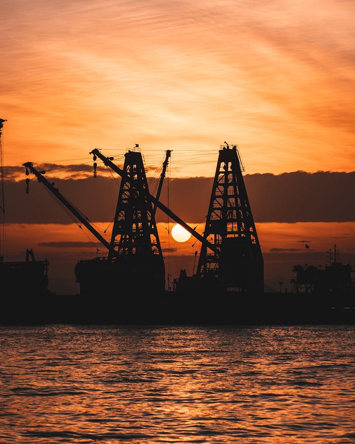 Crafting Captivating Headlines: Your awesome post title goes here Silhouetted cranes at a shipyard during a stunning sunset by the water.