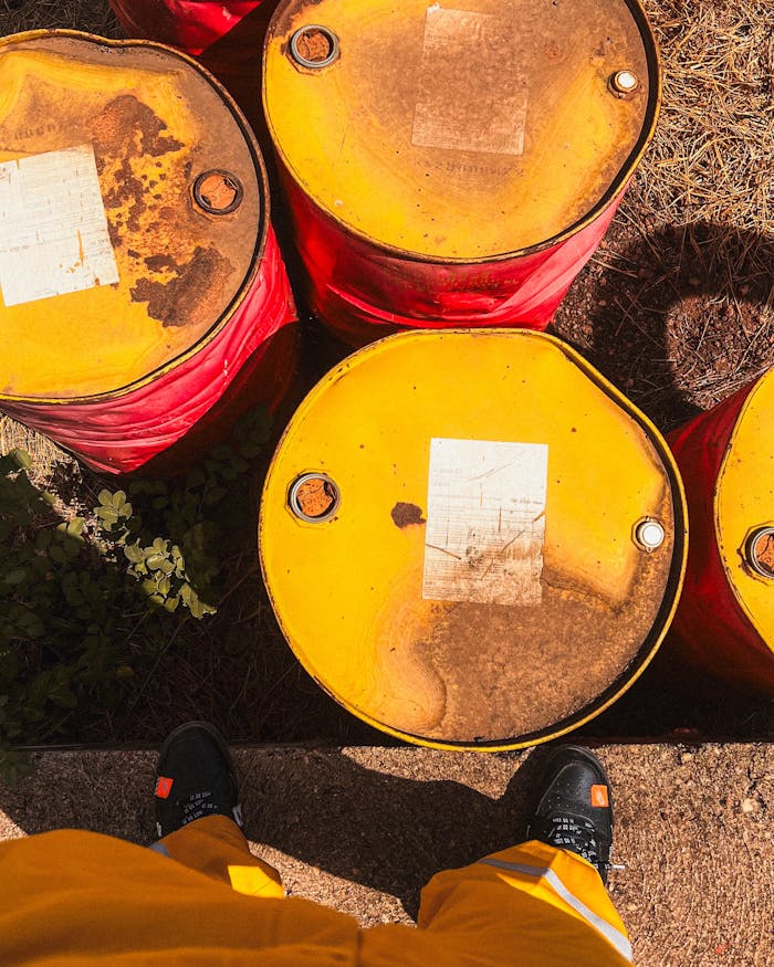 creative-01 Top view of weathered yellow oil barrels on ground, person visible wearing yellow pants.