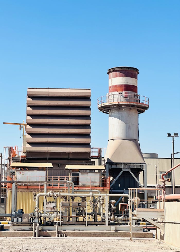 creative-02 Industrial power plant against a clear blue sky, featuring storage tanks and a chimney.